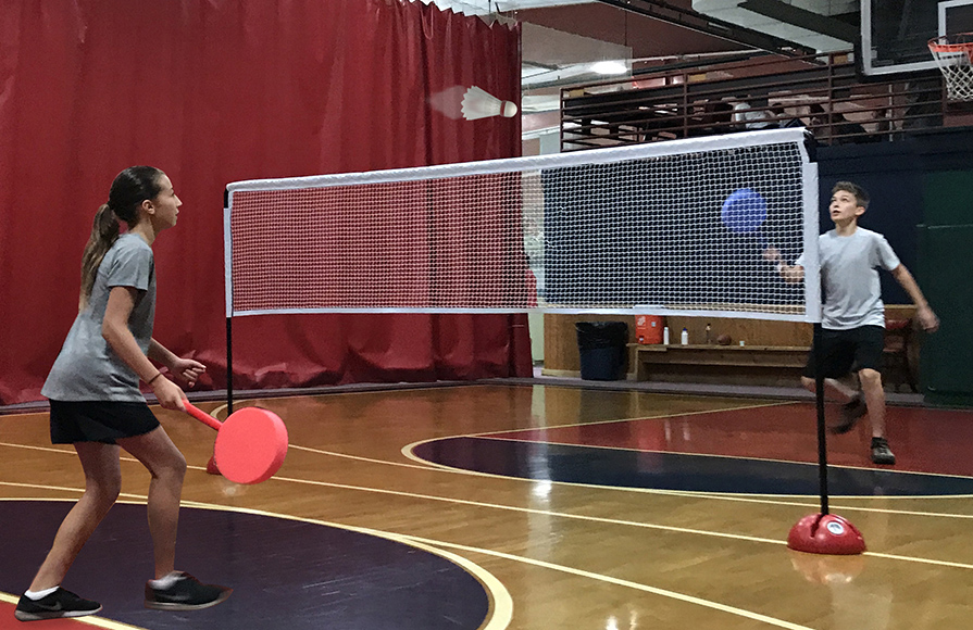 Two young teens with foam badminton paddles volleying a shuttlecock over a multi-dome dual net set as a badminton net